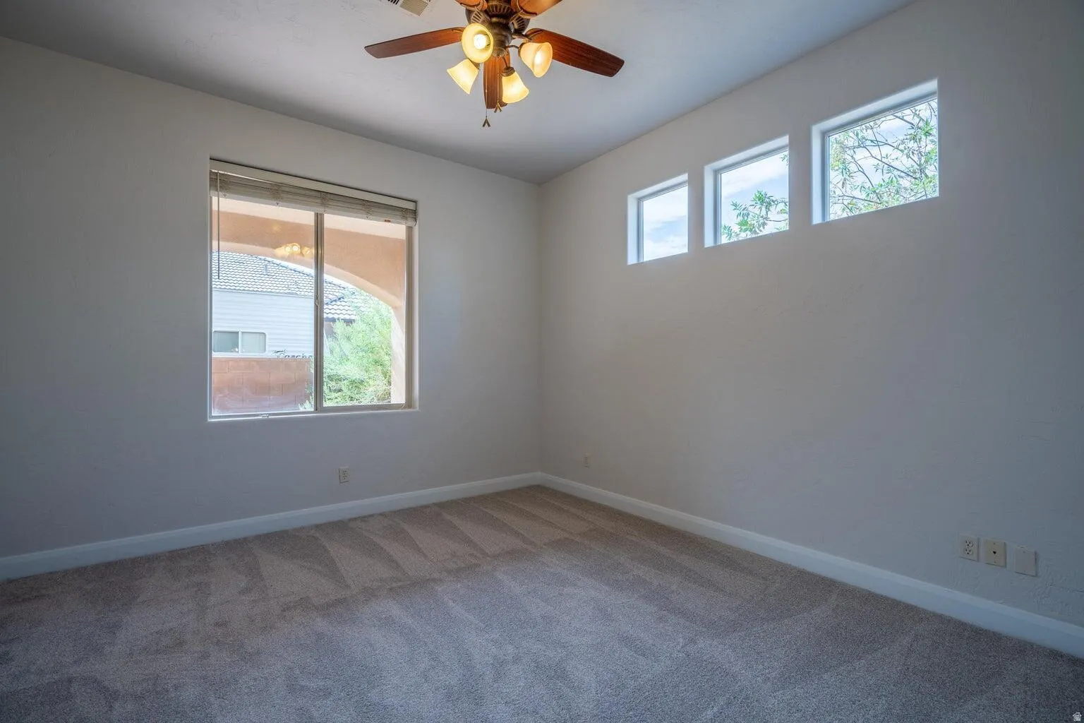 Neutral wall paint, plush carpet flooring, a ceiling fan with light fixture, a large window, and three high-set transom windows