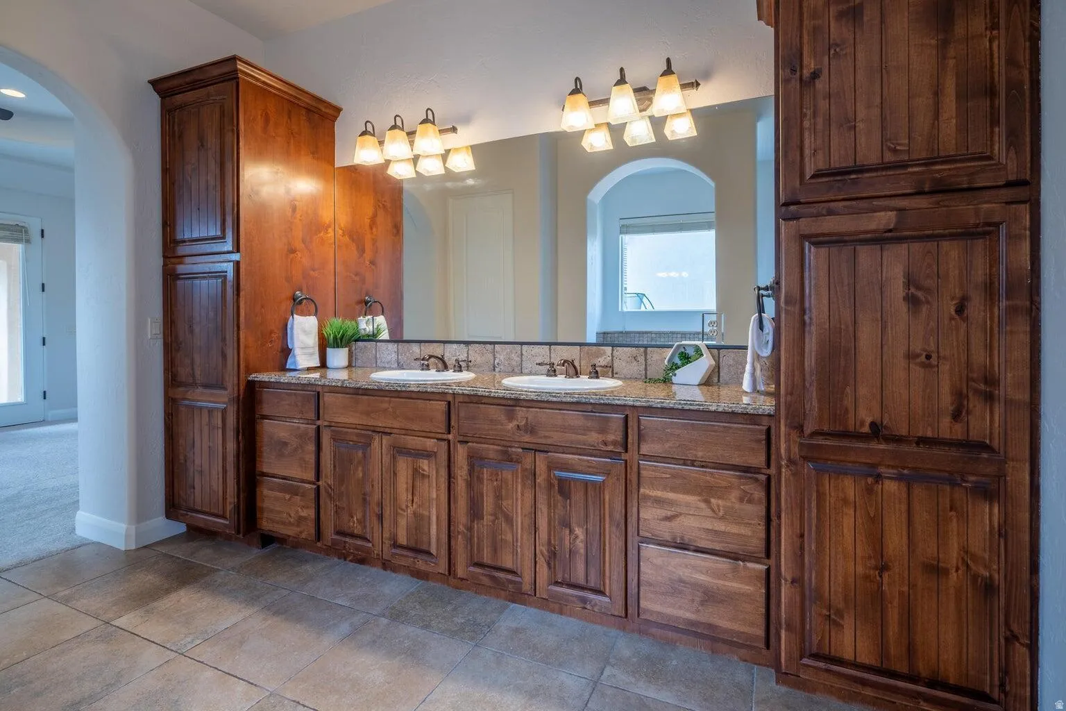Dual vanity with wood-finish cabinetry, granite-style countertop, and integrated sinks