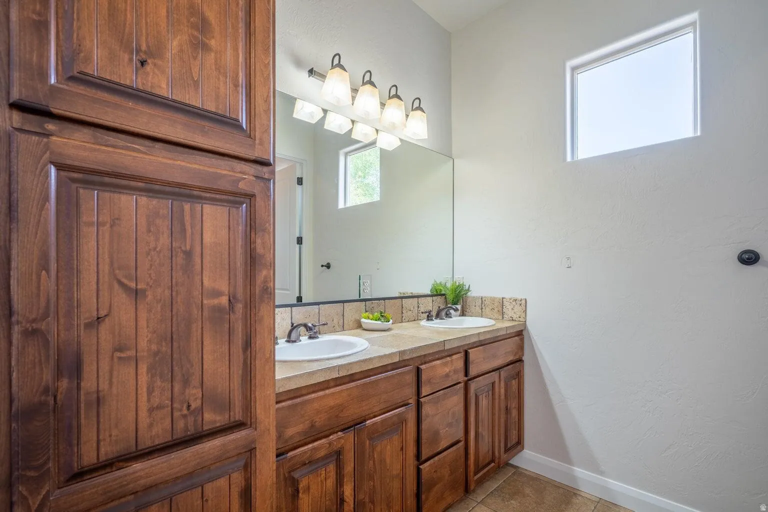 Bathroom featuring a dual vanity with light-colored countertops, wood-finish cabinetry, and built-in vertical storage
