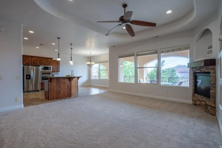 Open-concept living area featuring a stone-faced fireplace, a multi-pane window wall, and a tray ceiling with recessed lighting