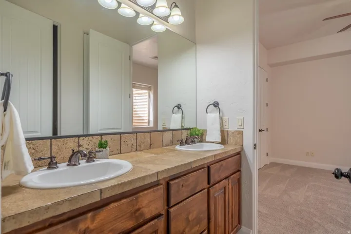 Dual vanity with integrated sinks, wood cabinetry, stone-finish countertop, and tiled backsplash