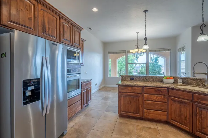 Kitchen featuring stainless steel appliances, wood cabinetry, granite countertops, and tiled flooring