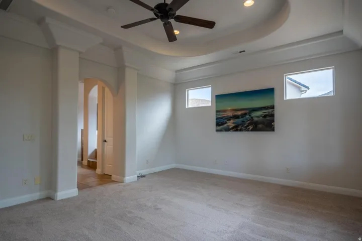 Spacious room featuring a tray ceiling with recessed lighting and a ceiling fan, carpet flooring, transom windows, and an arched entry