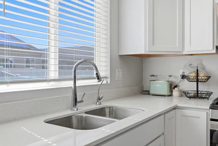 Kitchen featuring white shaker cabinetry, light-toned countertops, a stainless steel double basin sink, and a chrome pull-down faucet