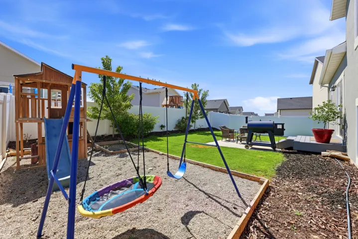 Manicured backyard featuring a wooden playset, a swing set on a gravel base, a dedicated patio area, and an elevated deck