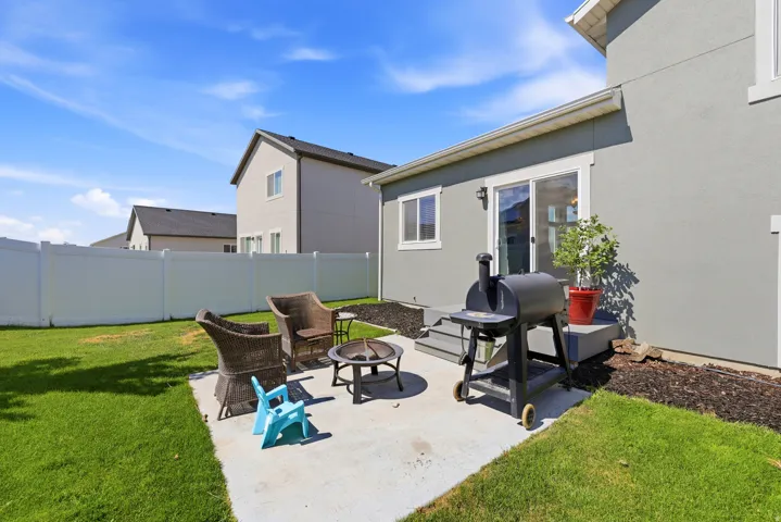 Private backyard featuring a concrete patio, sliding glass door entry, full vinyl fencing, and a manicured lawn
