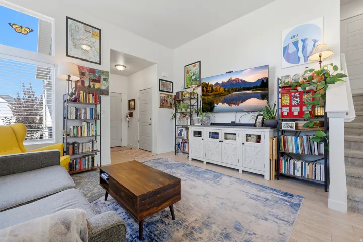 Spacious living area featuring high ceilings, light wood-finish flooring, and natural light from large windows