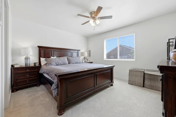 Bright bedroom featuring neutral-toned carpet flooring, a ceiling fan with integrated lighting, and a large window with blinds