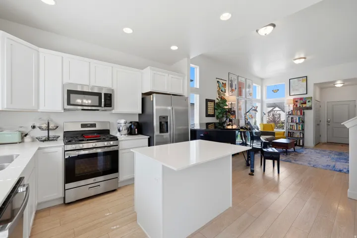 Open-concept living space featuring a modern kitchen with white cabinetry, stainless steel appliances, a center island with a solid surface countertop, and wood-finish flooring throughout
