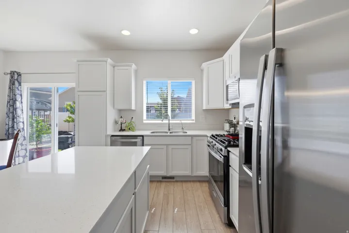 Kitchen featuring white cabinetry, stainless steel appliances, a large island with a light-colored countertop, and wood-finish flooring
