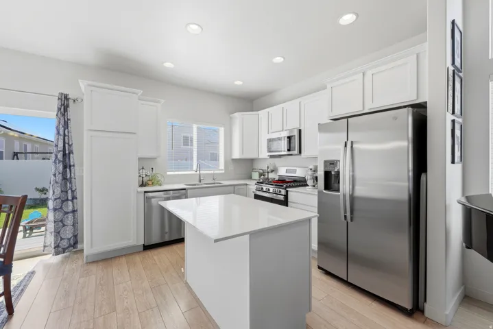 Contemporary kitchen featuring white cabinetry, stainless steel appliances, light wood-finish flooring, recessed lighting, and a center island with a quartz countertop