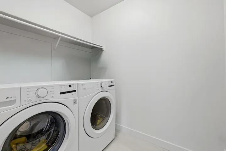Dedicated laundry area featuring a washer and dryer set, overhead shelving, and light-toned walls