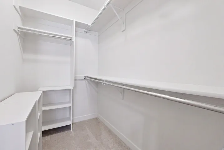 Walk-in closet featuring built-in shelving, multiple hanging rods, and light-toned carpeting