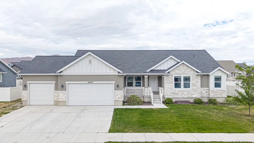 Ranch-style residence featuring a gray exterior with stone accents, a dark shingle roof, a two-car garage with an additional single-car garage, and a covered front porch with white railing