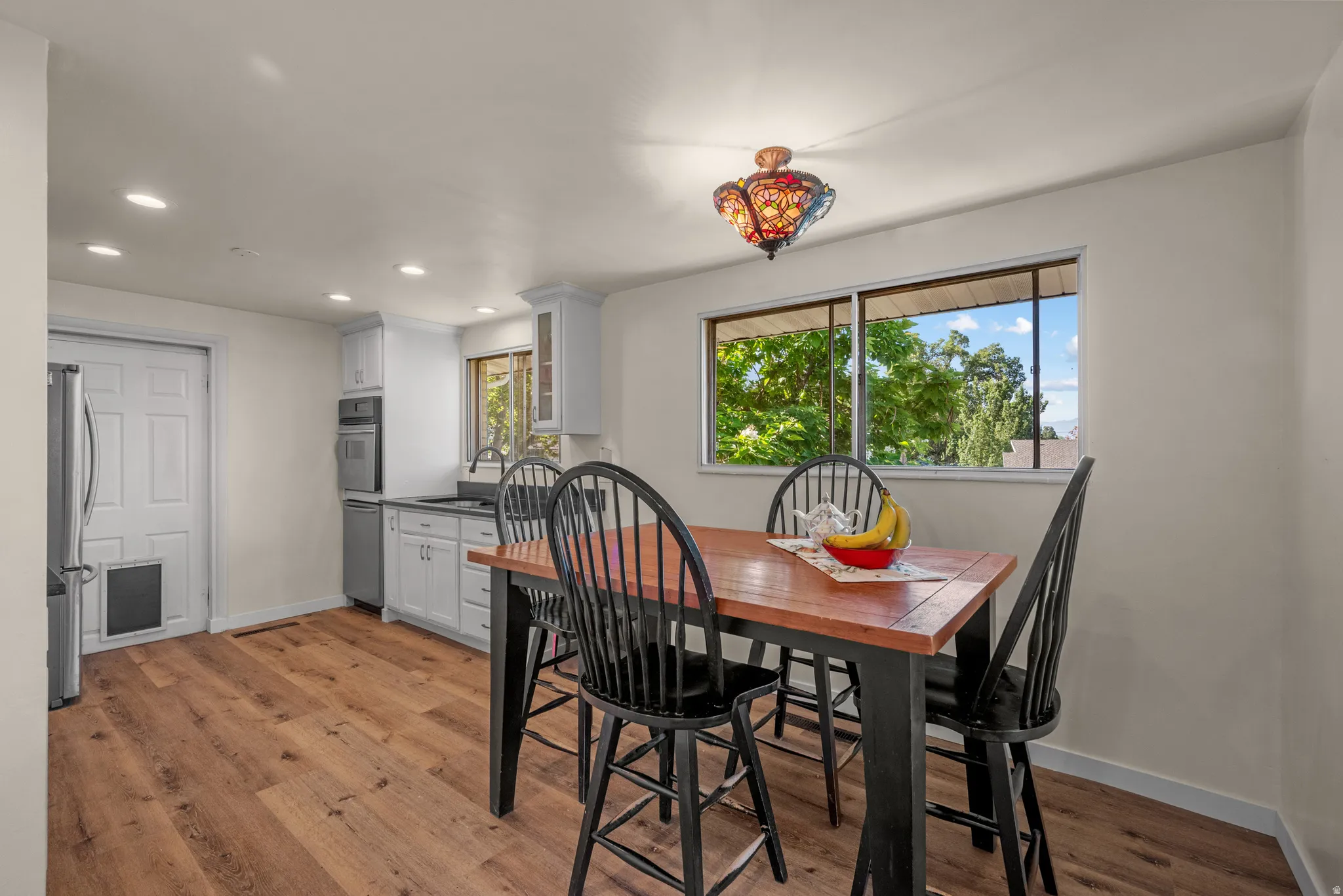 Open-concept dining area featuring wood-finish flooring, a window with exterior tree views, and a decorative ceiling light fixture