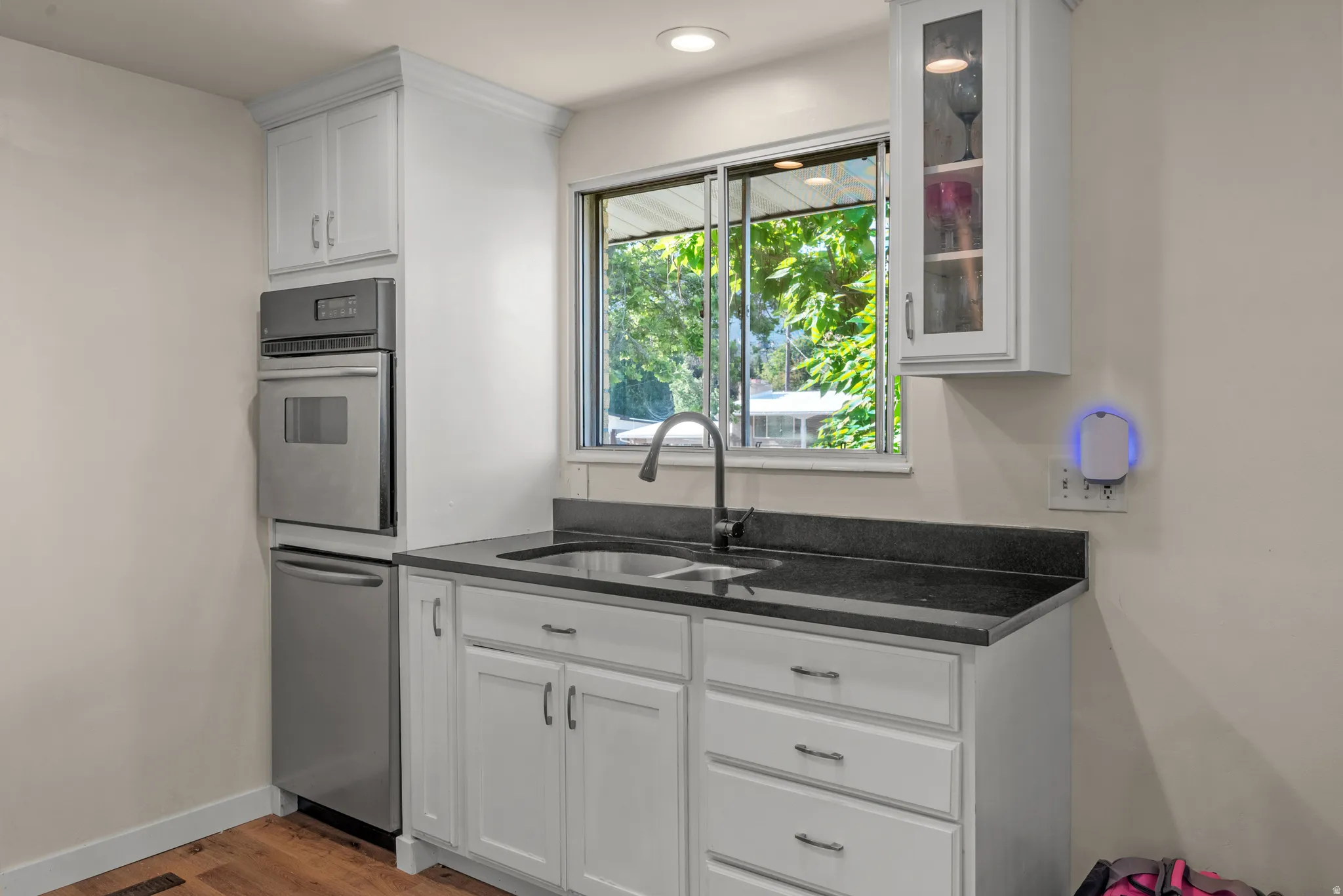 Kitchen area featuring white cabinetry, dark countertops, a stainless steel wall oven, and an integrated dishwasher