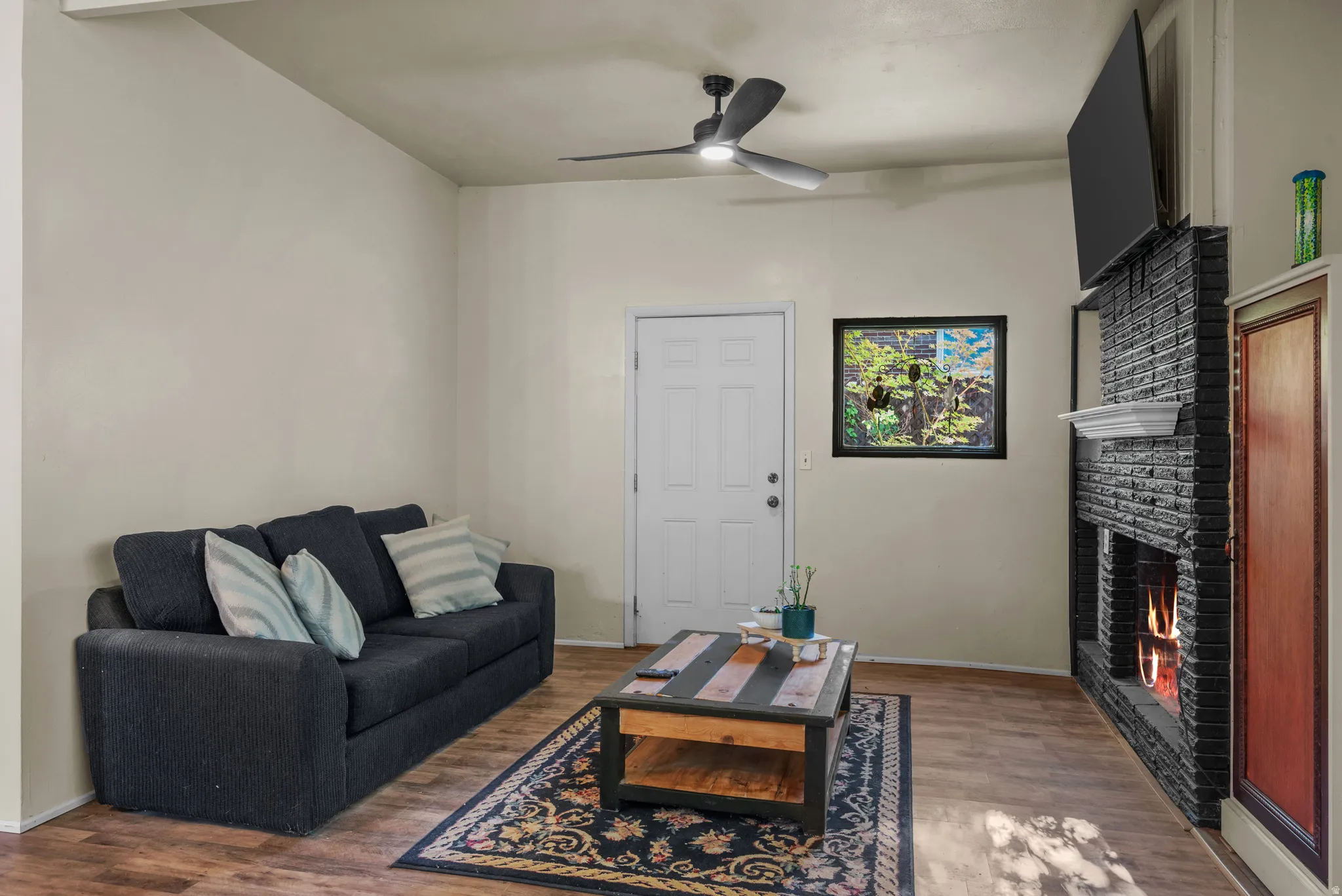 Living area featuring wood-finish flooring, a contemporary ceiling fan, and a black brick fireplace with a white mantel