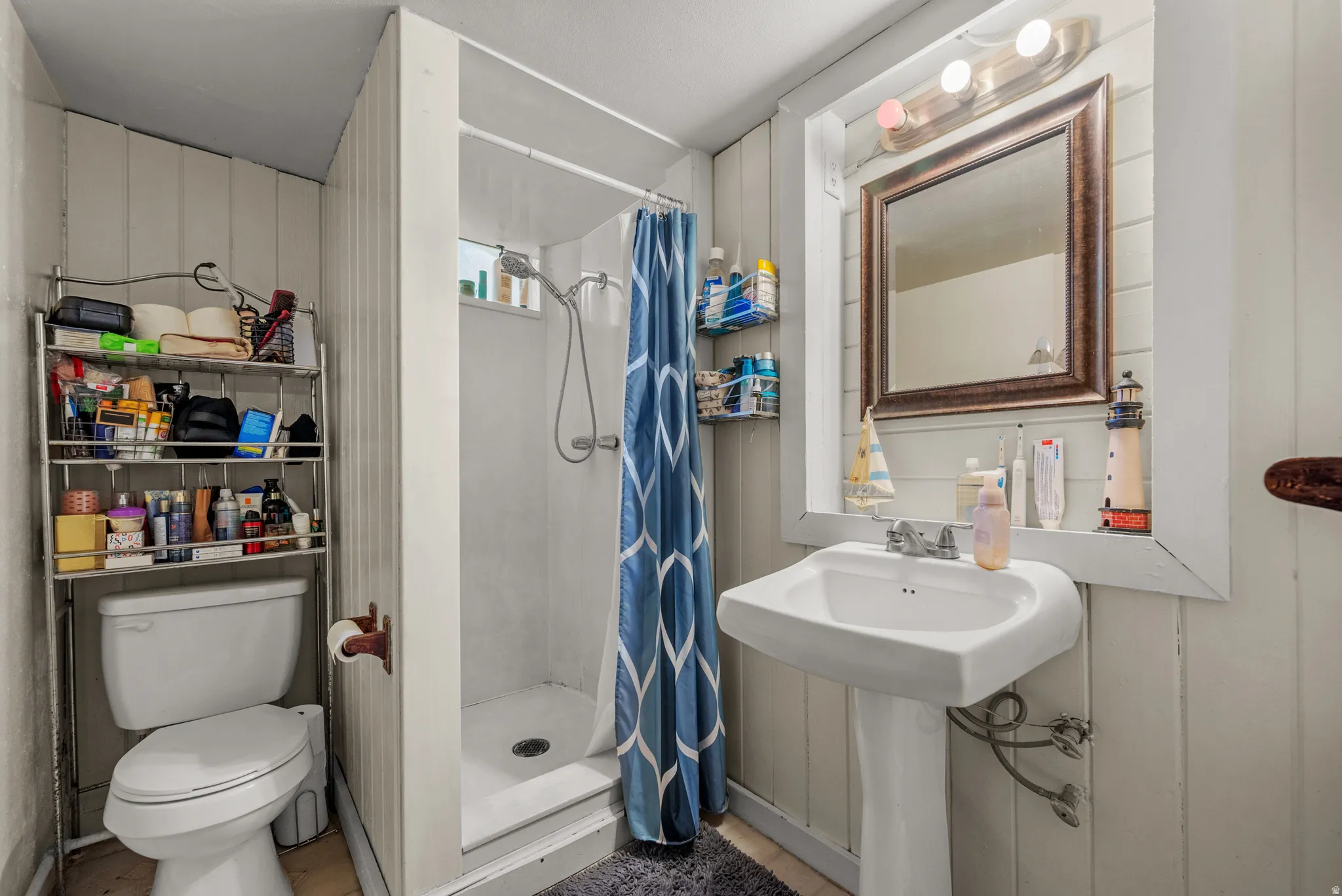 Pedestal sink with framed mirror, a built-in shower stall, and vertical paneling