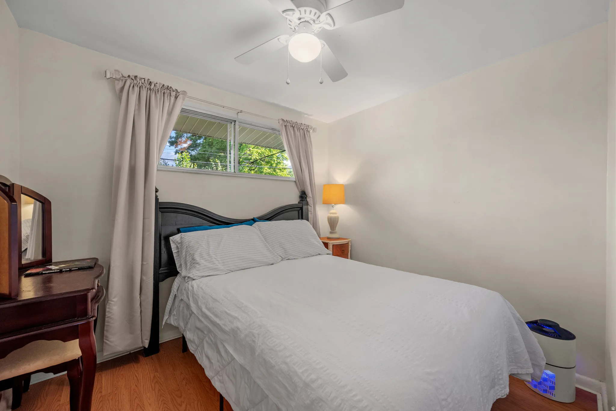 Room featuring wood-finish flooring, a ceiling fan with light fixture, and windows providing natural illumination