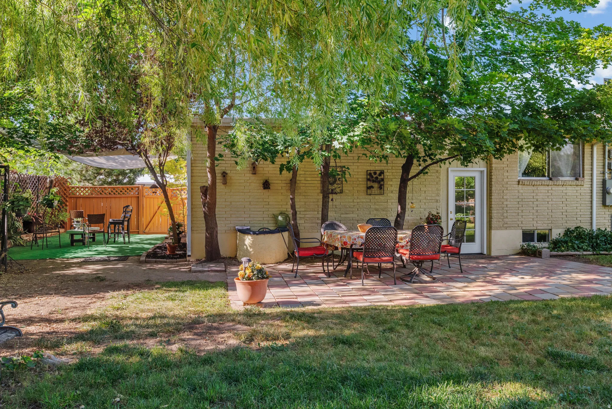 Expansive backyard featuring a brick paver patio, mature trees, and a wooden privacy fence