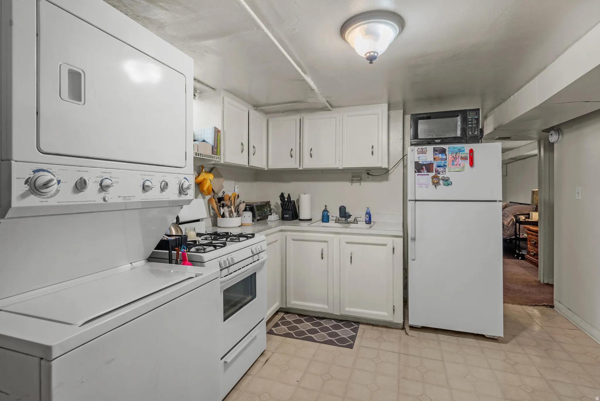 Compact kitchen area featuring a gas range, white cabinetry, and a stacked washer and dryer unit
