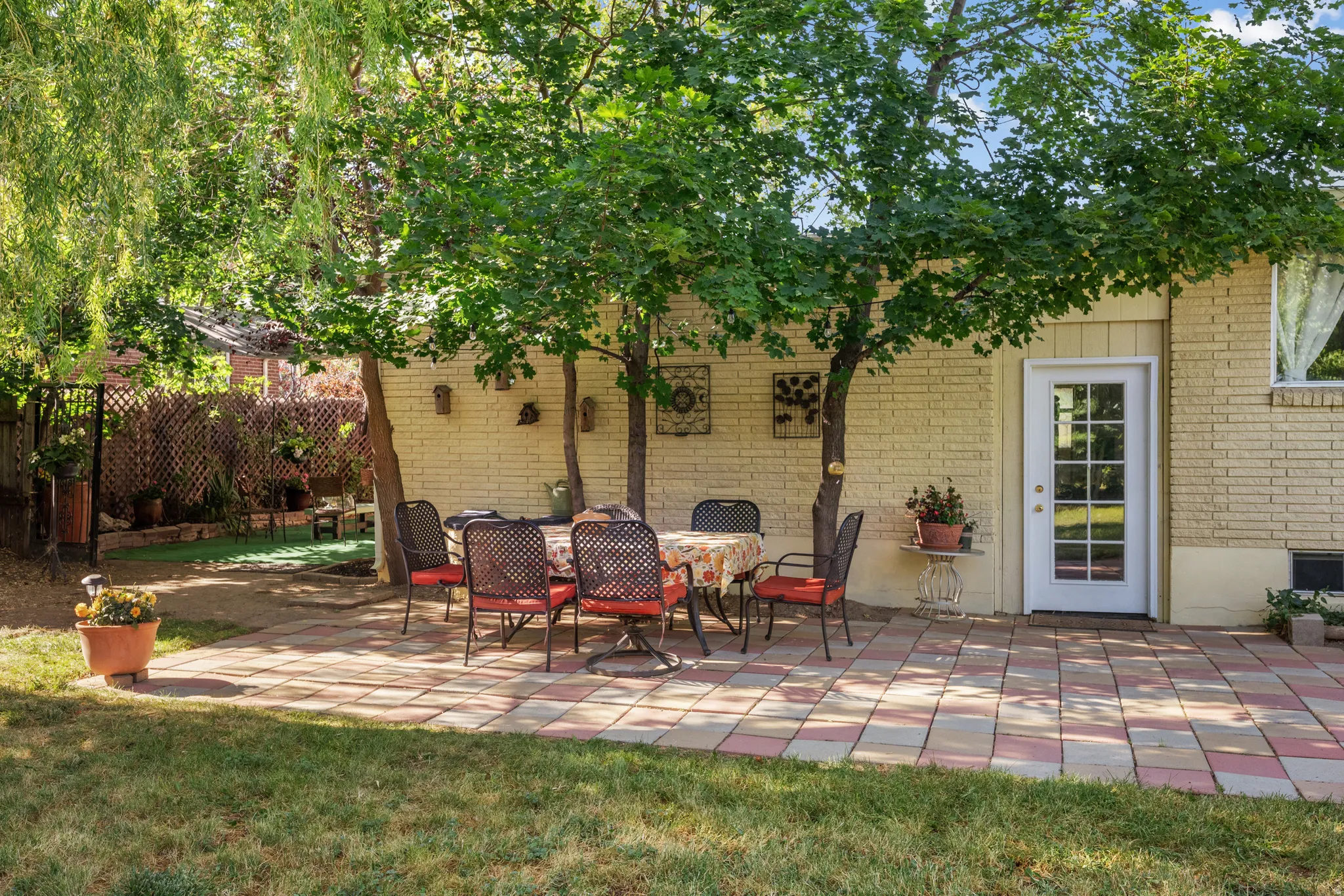 Paved patio area featuring multi-toned pavers, mature shade trees, and a brick exterior wall