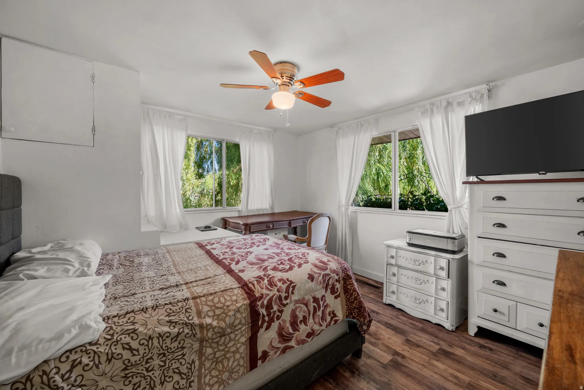 Bedroom featuring wood-finish flooring, two window openings with white trim, and a ceiling fan with integrated lighting