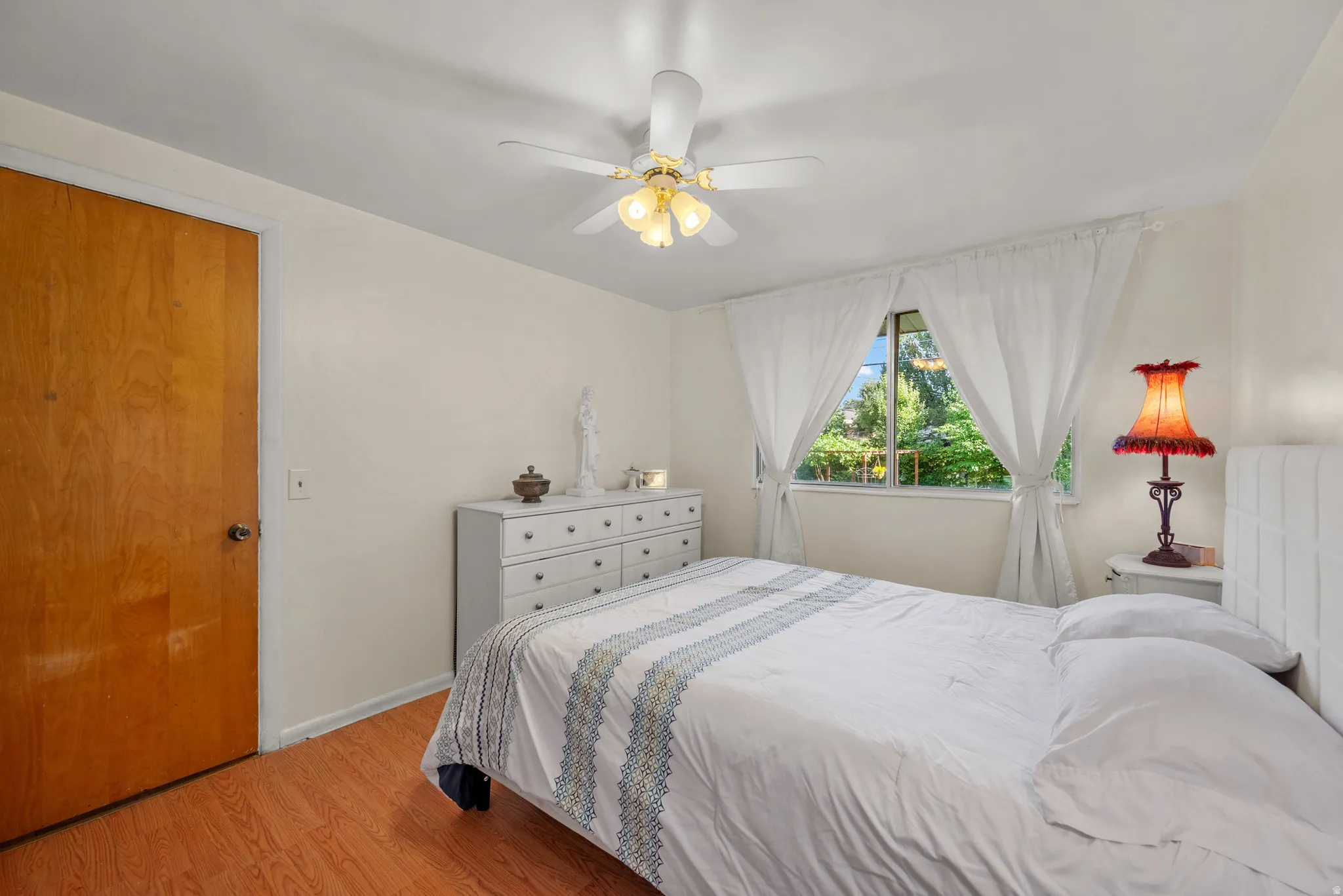 Bedroom featuring wood-finish flooring, a window with exterior tree views, and a ceiling fan with integrated lighting