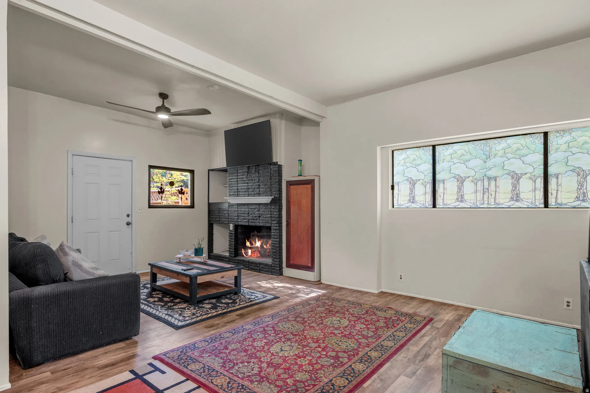 Living space featuring wood-finish flooring, a contemporary fireplace with a stacked stone facade, integrated shelving, and a ceiling fan