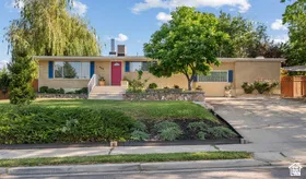 Split-level residence featuring a vibrant red front door, blue window shutters, and a well-maintained front lawn with mature trees