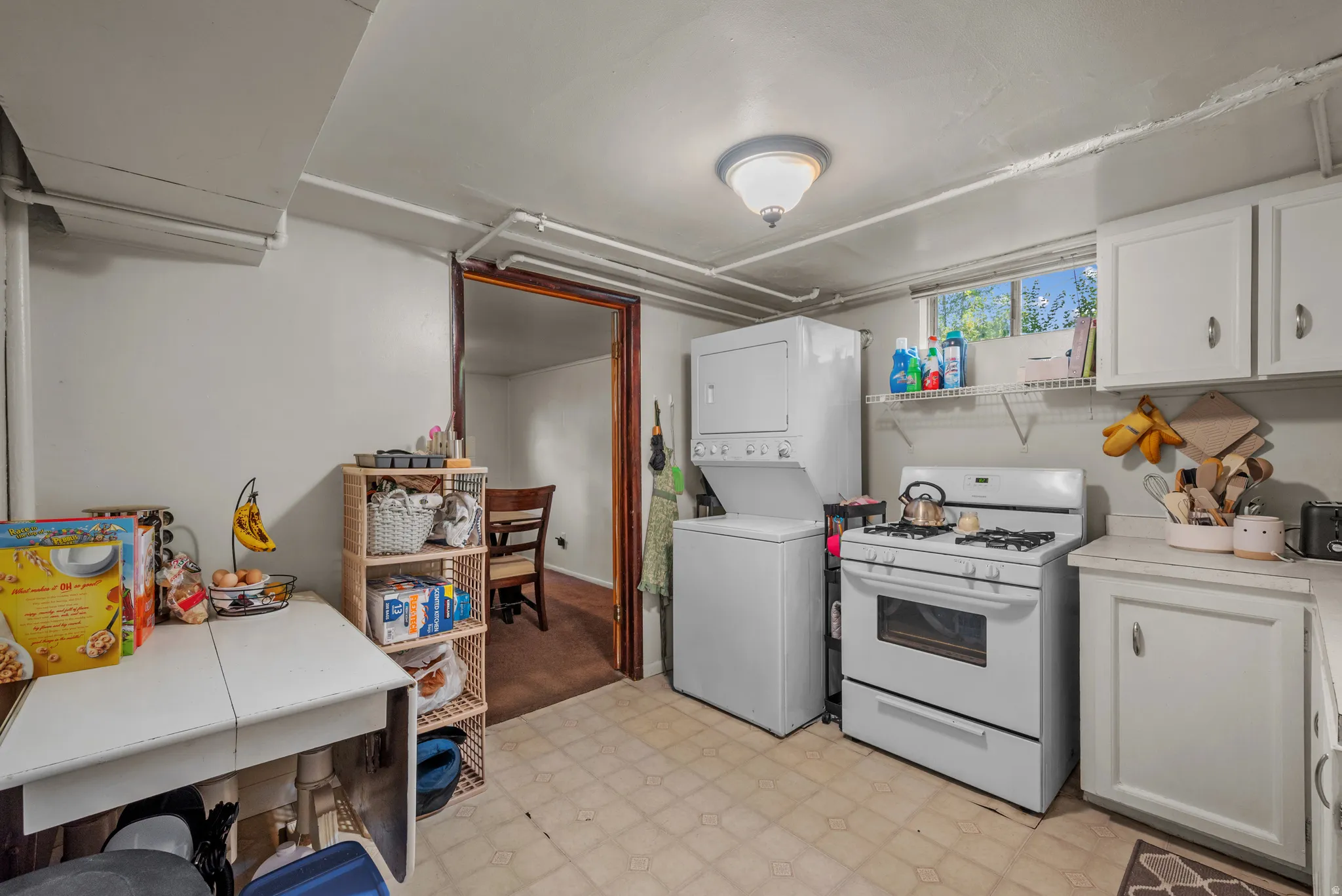 Utility space featuring a gas range, white cabinetry, and a stacked washer and dryer unit