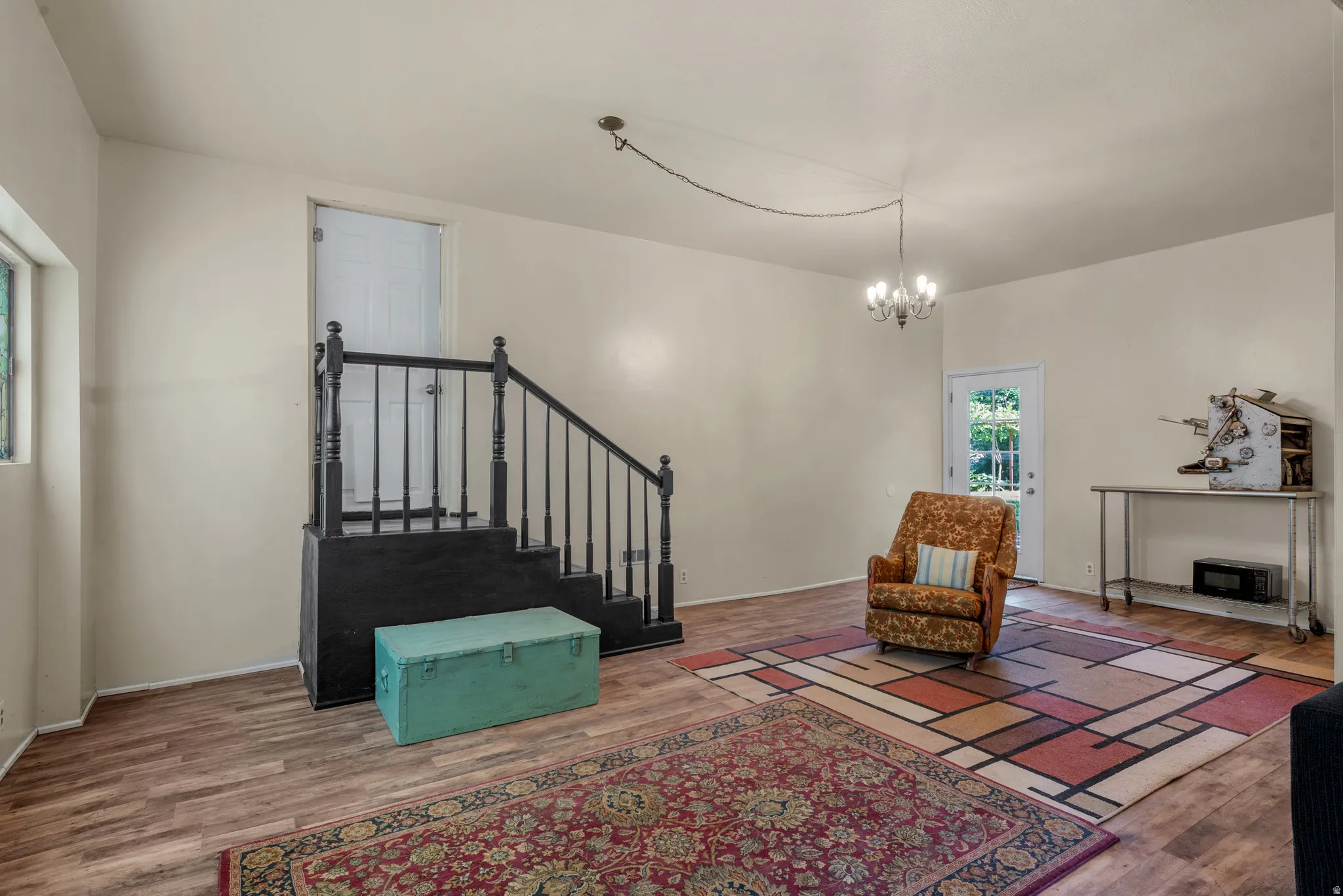 Spacious room featuring wood-finish flooring, light-toned walls, and a prominent staircase with black banisters
