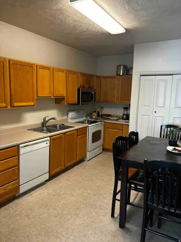 Kitchen featuring wood cabinetry, laminate countertops, a double basin stainless steel sink, a microwave, and a dishwasher