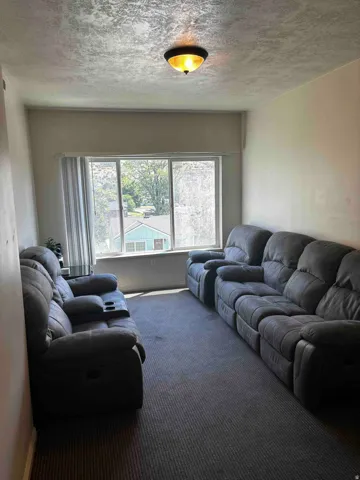 Comfortable den or recreation room featuring dual reclining seating, neutral carpeting, and abundant natural light from a sliding glass door with thermal-pane windows