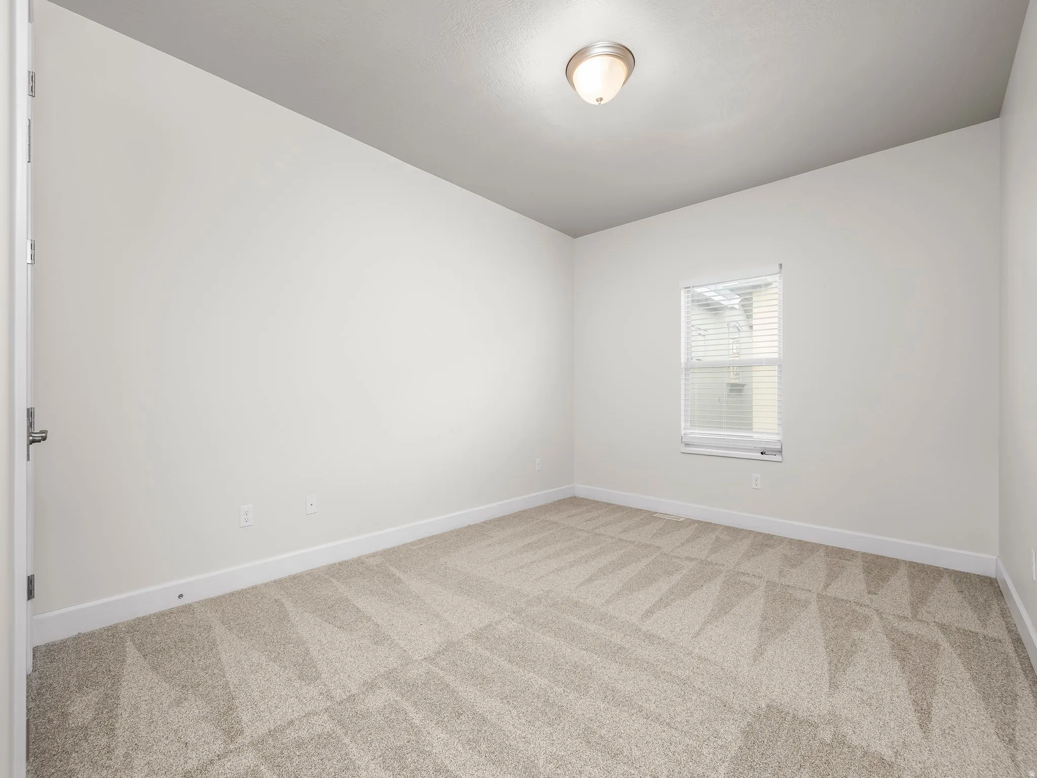 Carpeted room featuring a single window with blinds, white baseboards, and a flush mount ceiling light