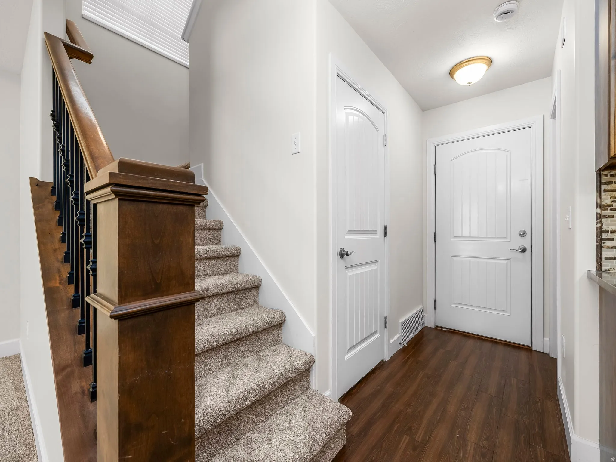 Entryway featuring wood-finish flooring, a white paneled door, and a staircase with wood newel post and baluster details