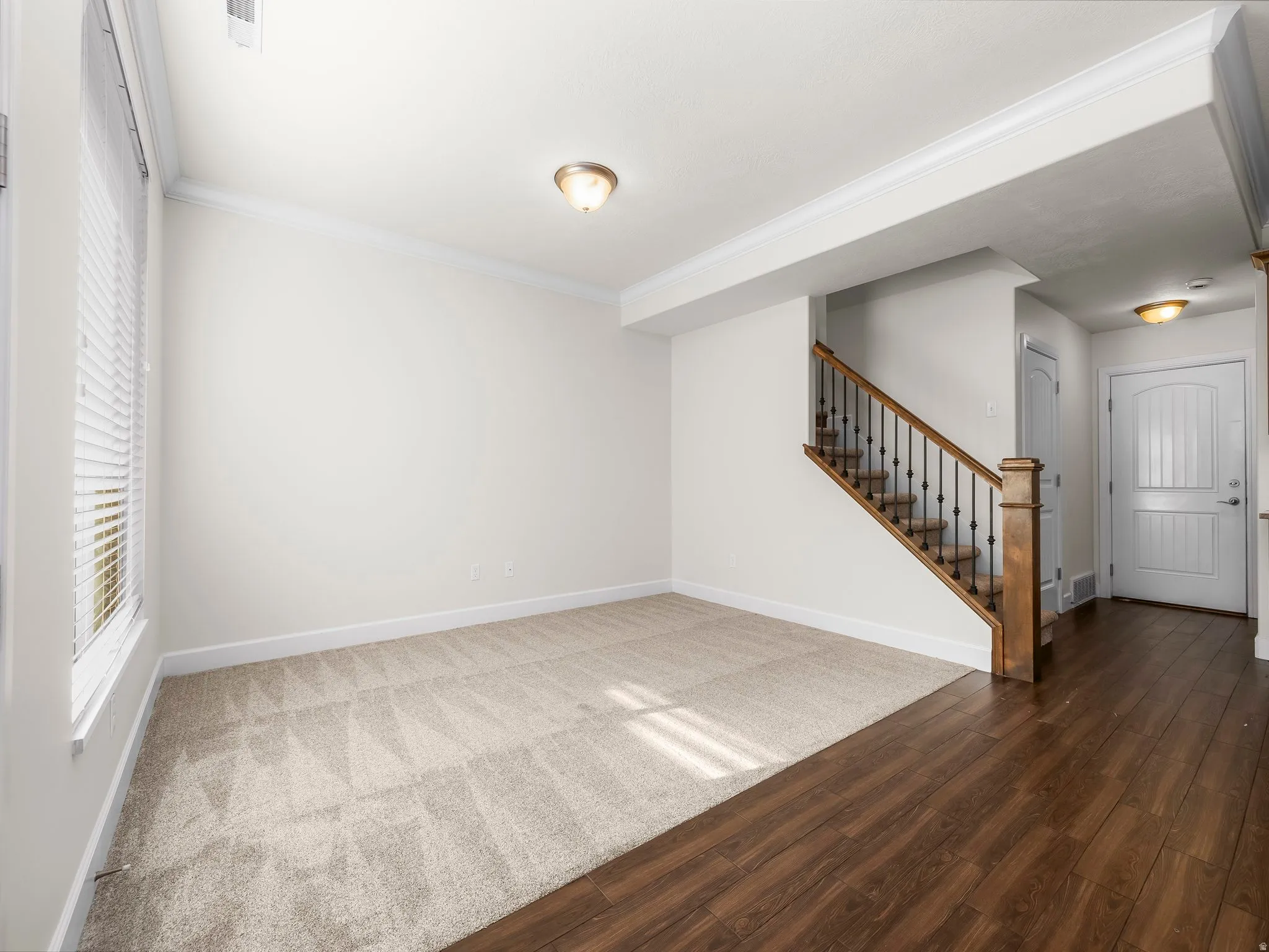 Open concept living area with light beige carpeting and crown molding