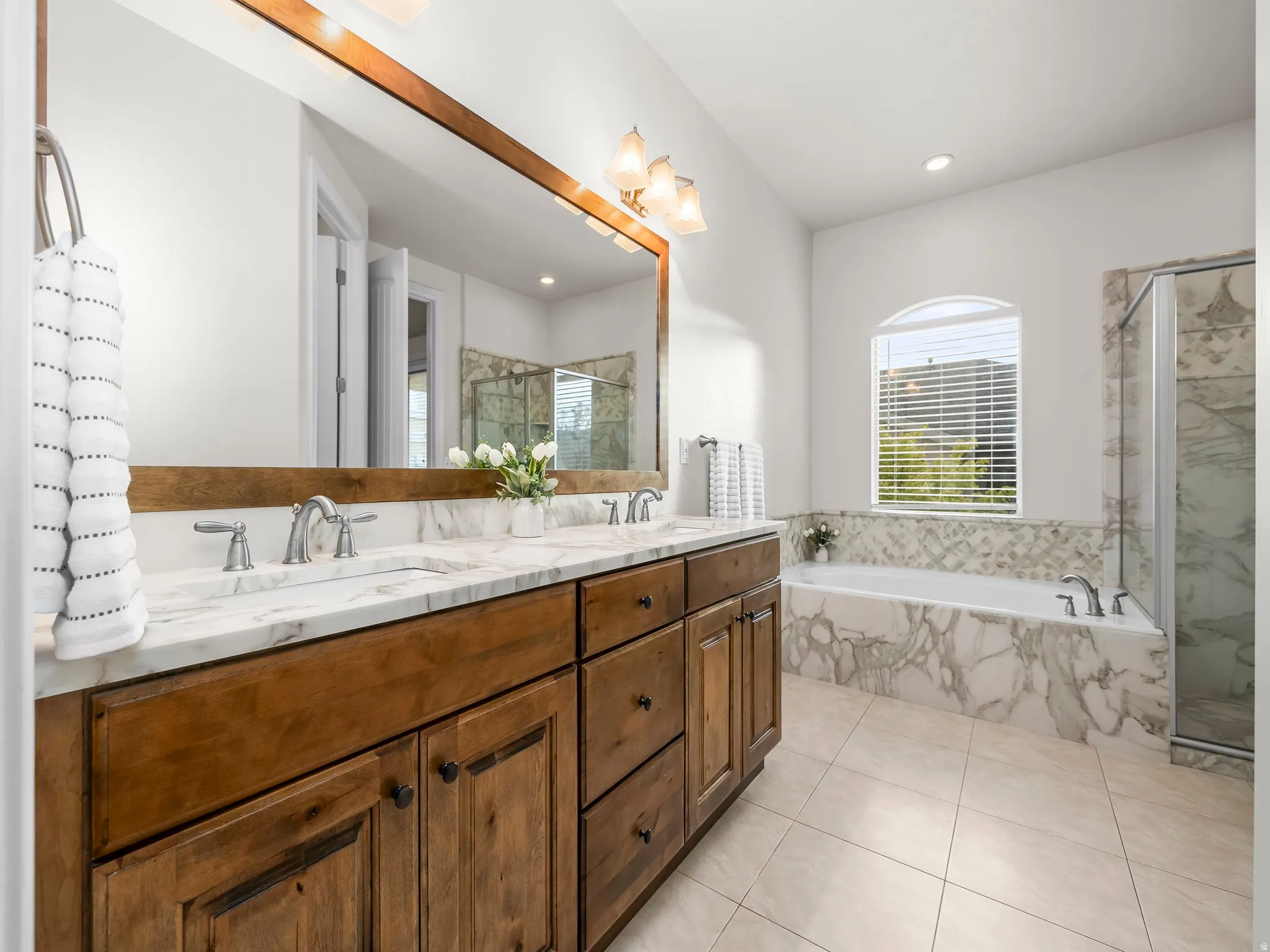 Bathroom vanity featuring a dual sink with a white stone countertop, warm wood-finish cabinetry, and a large framed mirror