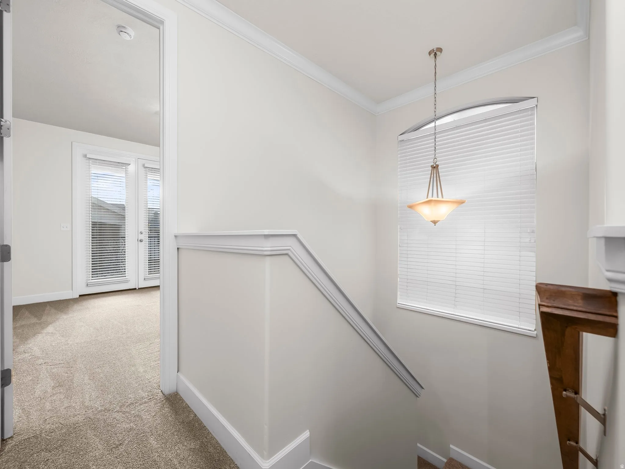 Stairwell featuring a bronze pendant light, arched window with horizontal blinds, and a wood-finish handrail