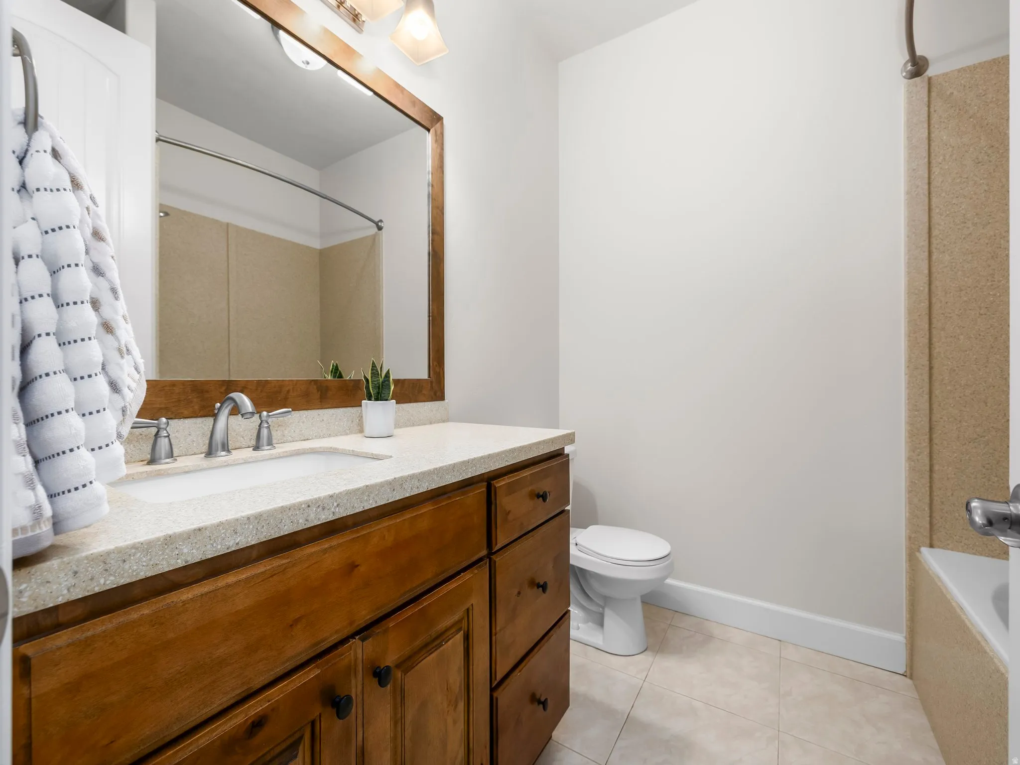 Bathroom featuring a wood-finish vanity with an integrated sink, a speckled countertop, and a framed mirror with overhead lighting