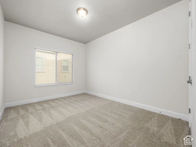 Neutral-toned room featuring a window with horizontal blinds, overhead lighting, and patterned carpet flooring