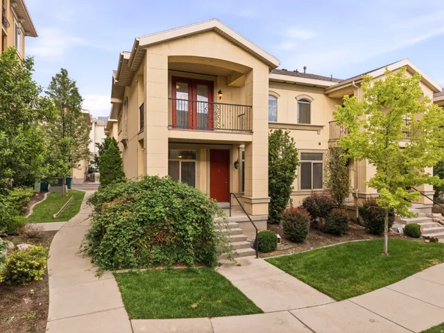 Multi-level stucco exterior featuring a prominent red entry door, a second-story balcony with iron railings, and arched windows