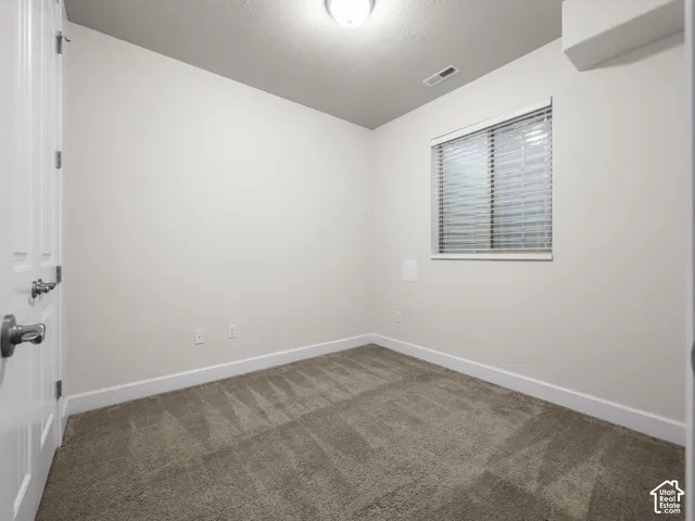 Neutral-toned room featuring wall-to-wall carpeting, a single window with horizontal blinds, and a flush-mount ceiling light fixture
