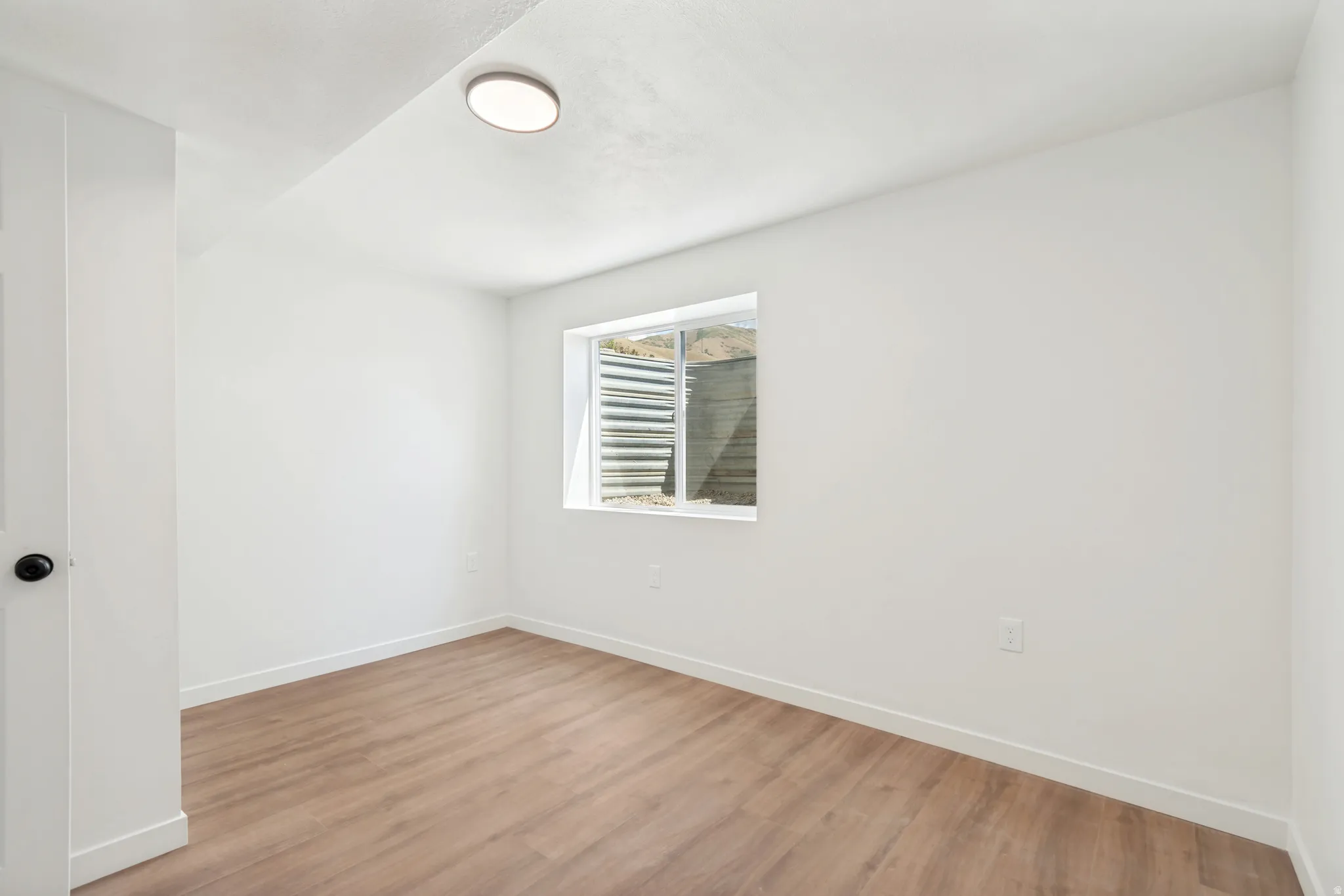 Bright room featuring light wood-finish flooring, white walls, and a single window
