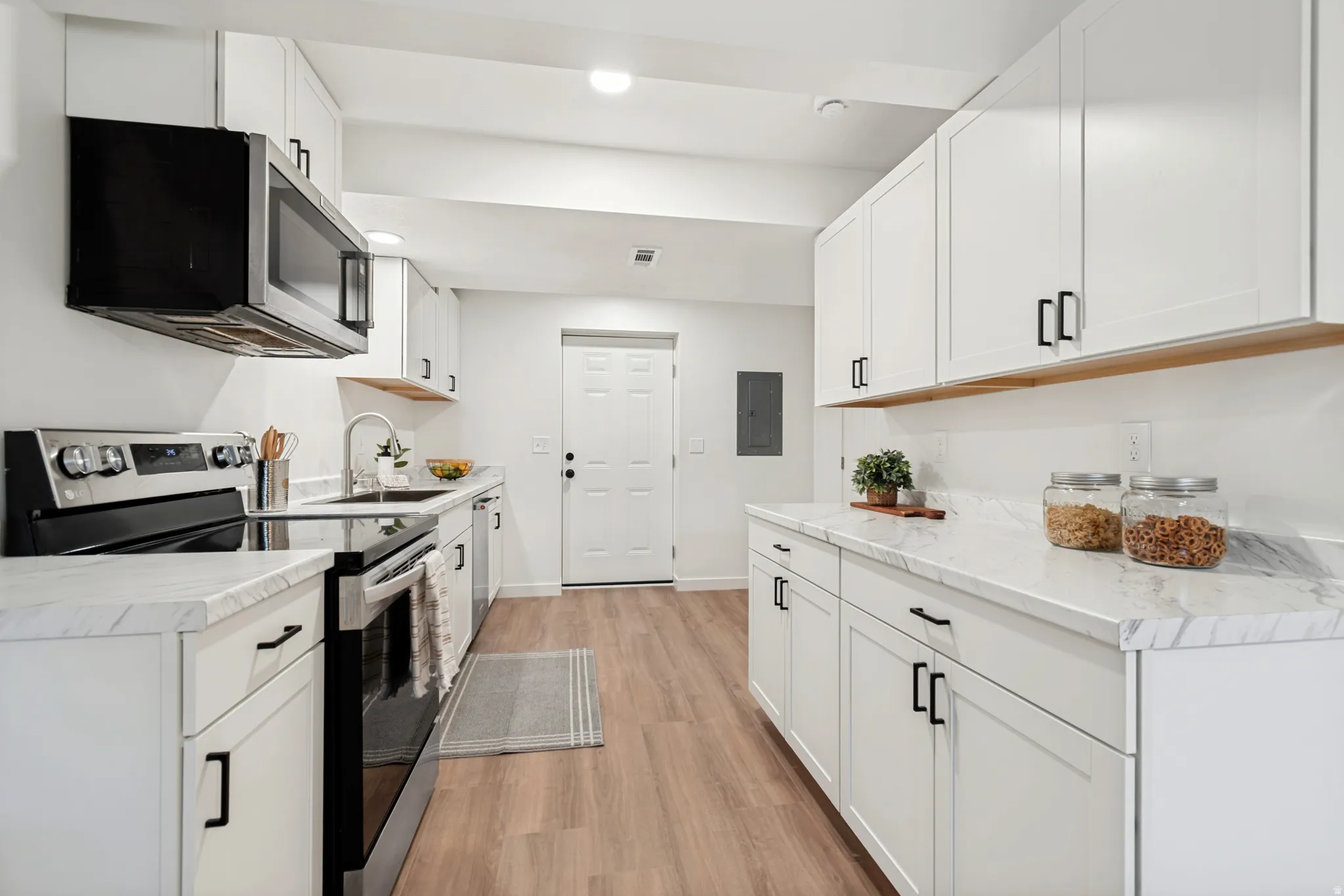 Modern kitchen featuring white shaker cabinetry, stainless steel appliances, marble-look countertops, and wood-finish flooring