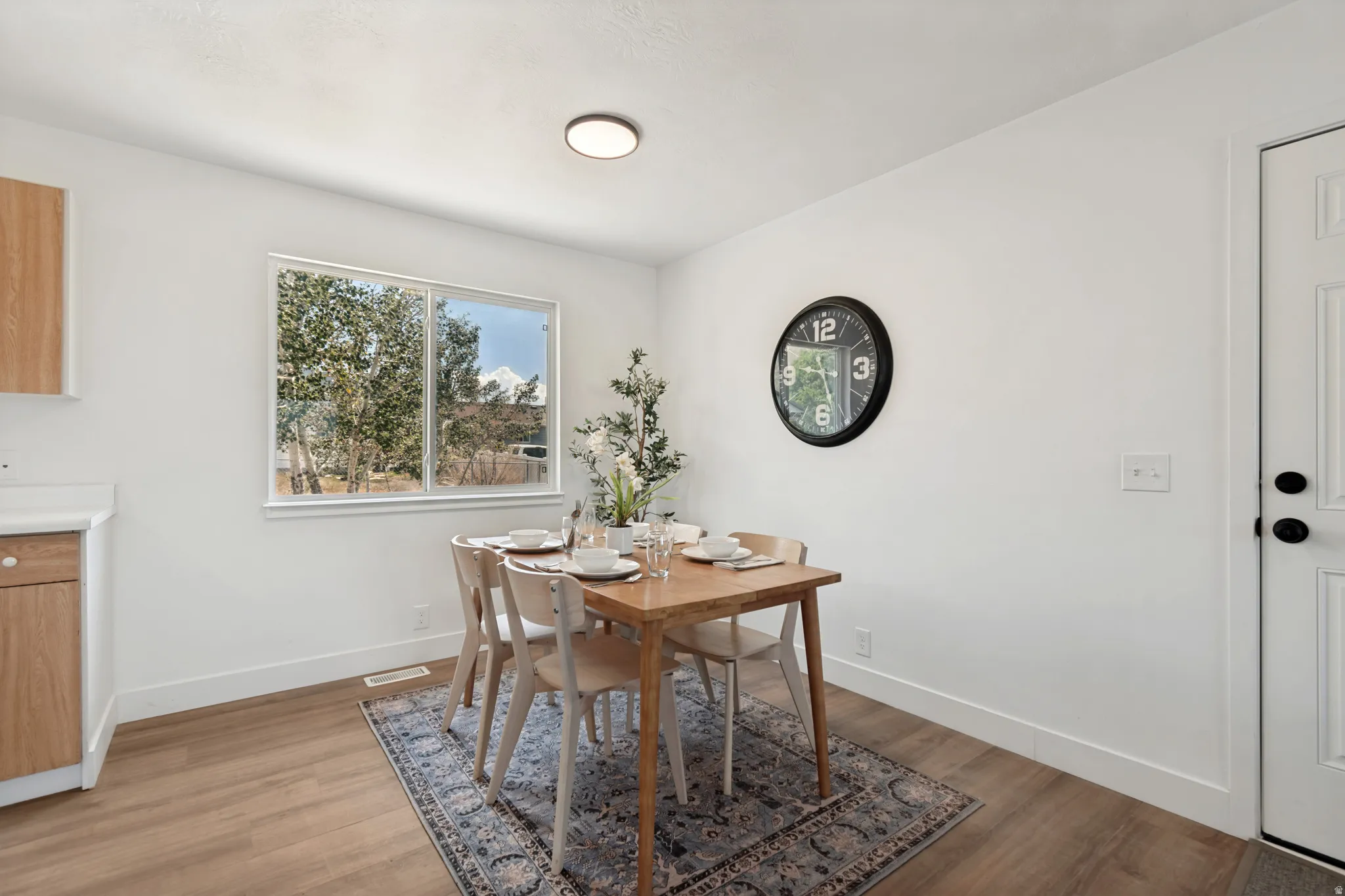 Bright dining area featuring wood-finish flooring, a contemporary flush-mount ceiling light, white baseboards, and a large window providing natural illumination