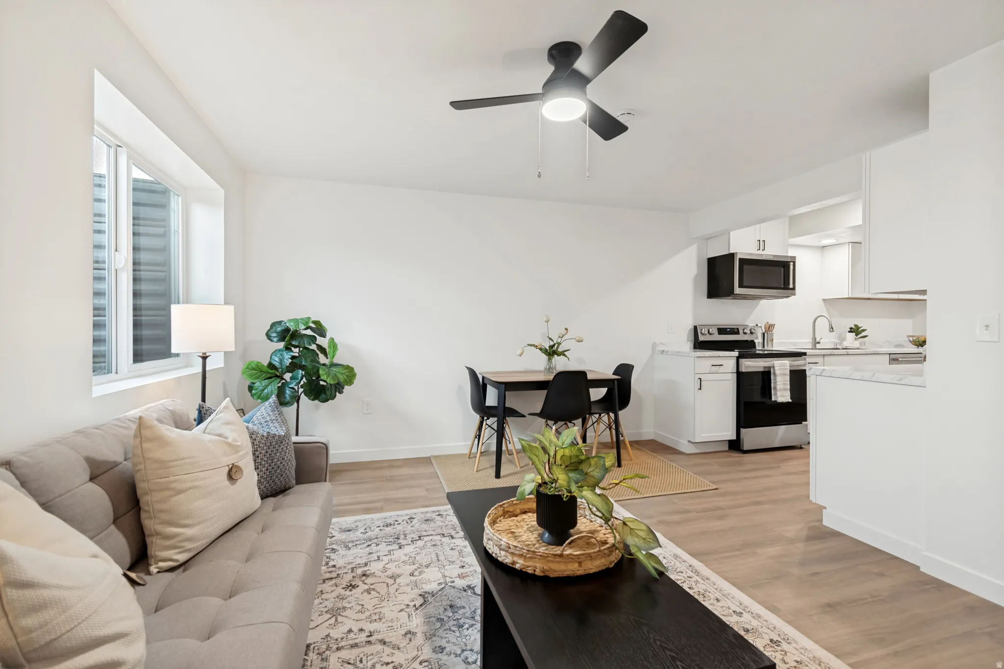 Open-concept living space featuring wood-finish flooring, white walls, and a black ceiling fan