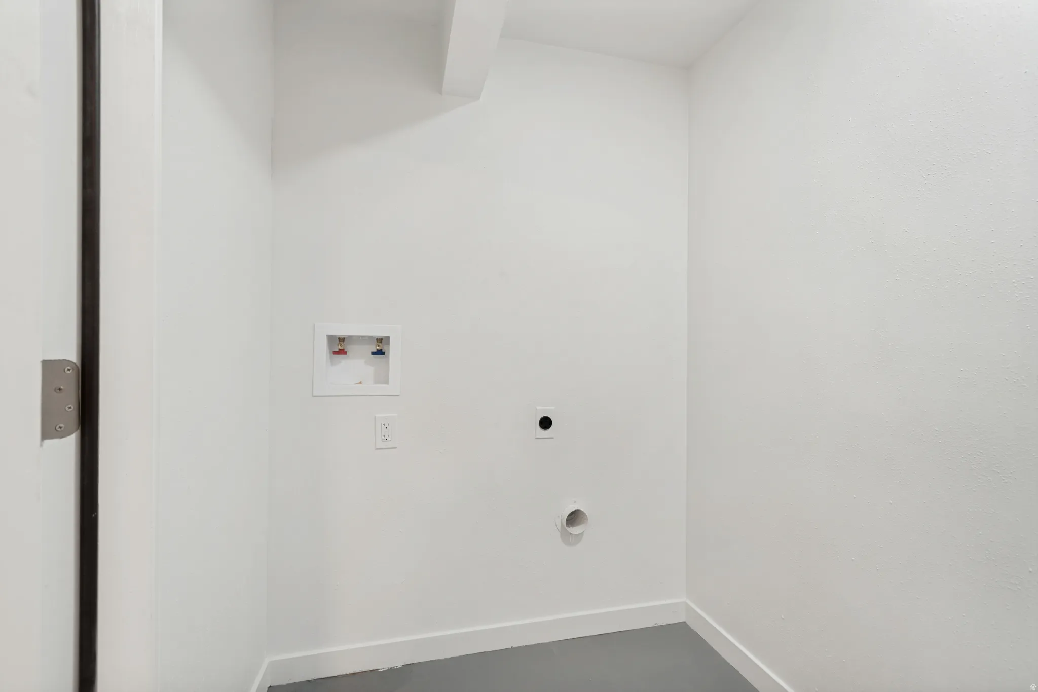 Laundry area featuring a wall-mounted water supply box and dryer vent, with a neutral gray floor and white baseboards
