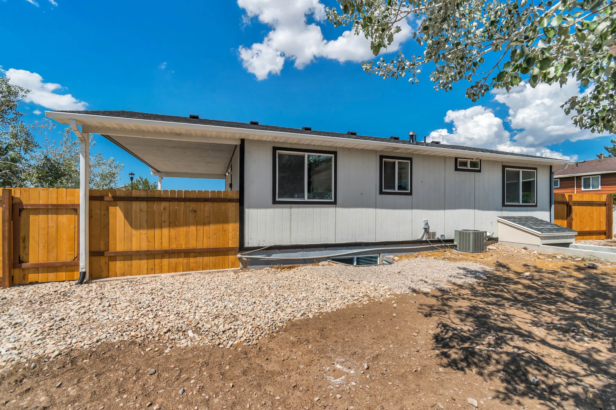 Rear exterior showcasing white siding with black trim windows, a covered patio area, and a wood fence