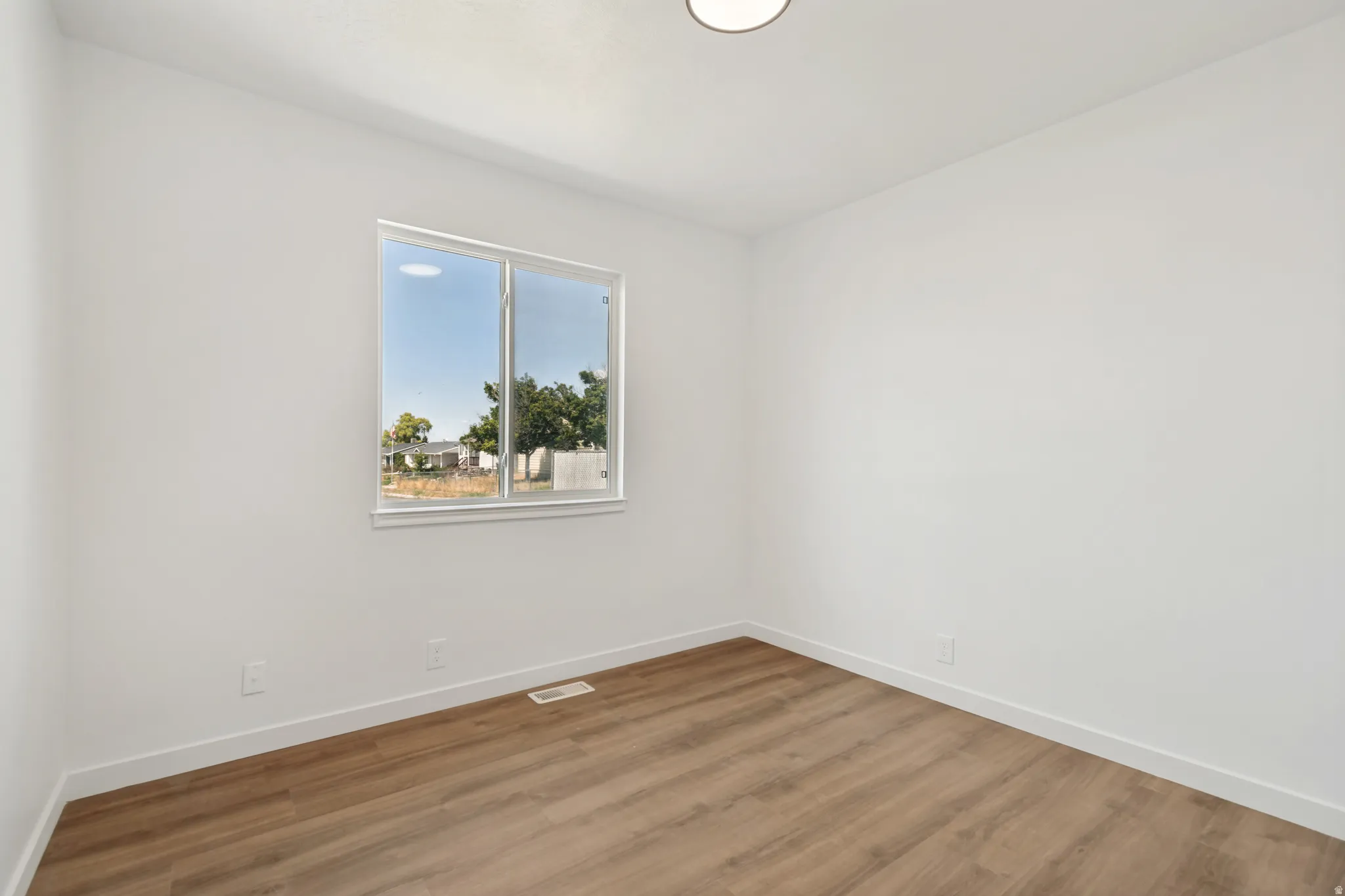 Room featuring wood-finish flooring, white baseboards, a white window frame, and a ceiling-mounted light fixture